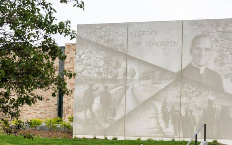 Large concrete mural outside with a tree next to it 